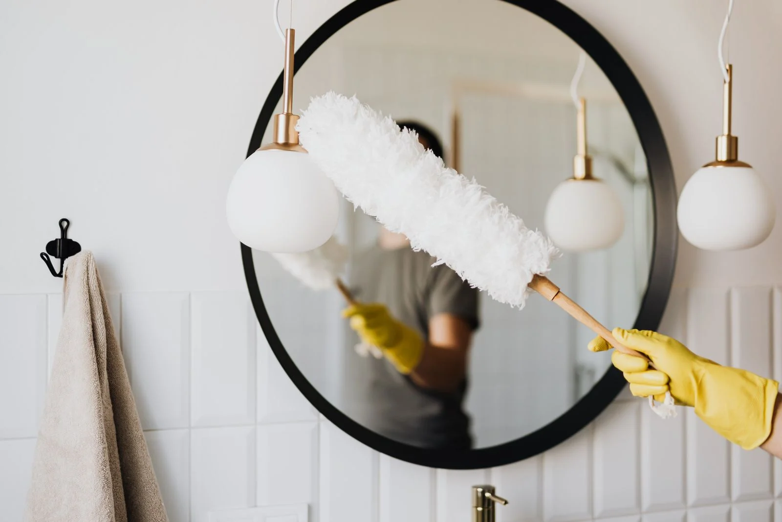 Cleaner dusting a mirror and surrounding fixtures
